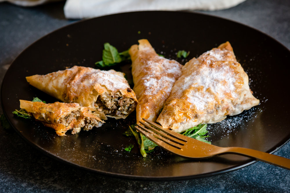 Meat filled triangular pastry on a plate with icing sugar